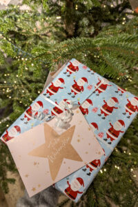 Wunschsternkarte an einem in Weihnachtspapier verpacktem Geschenk befestigt mit einem beleuchteten Tannenbaum im Hintergrund