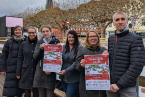 Die Organisatoren und Verantwortlichen des Weihnachtsmarktes Holzminden stehen mit Veranstaltungsplakaten zum Weihnachtsmarkt Holzminden vor der Eisbahn.