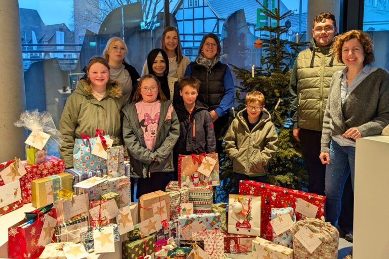 Isabell Adam vom Stadtmarketing posiert mit zwei Mitarbeiterinnen und sieben Kindern von der Stiftung Kinderheimat Neuhaus sowie mit 45 Geschenken vor dem Geschenkebaum in der Tourist-Information.