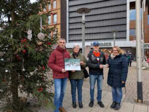 Matthias Kumlehn, Hanna Zota und Sascha Stein von der Holzmindener Tafel und Inga Schaper stehen neben dem "Little Ugly Chrisdtmas Tree" und dem Kaufhaus Schwager im Hintergrund.