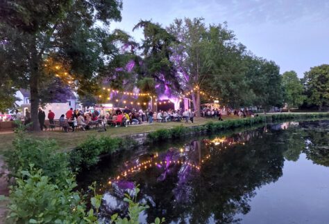 Blick über den Teich auf die am Ufer stehenden Sitzreihen mit der Bühne im Hintergrund.