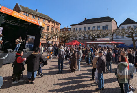 Foto vom gefüllten Marktplatz for der Kükenfest-Bühne bei strahlend blauem Himmel und Sonnenschein. Auf der Bühne musizieren Denny und Jens.
