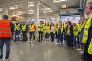 Foto einer großen Interessentengruppe in Wärmepumpen-Produktionshalle von Stiebel Eltron, die den Erklärungen von Pressesprecher Henning Schulz folgen.