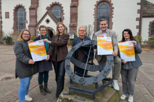 Die Veranstalter und Organisatoren des 49. Kükenfestes stehen mit Veranstaltungsplakaten auf dem Vorplatz der Lutherkirche.