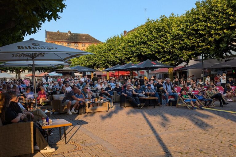 Blick auf einen vollen Marktplatz mit Menschen, die Livemusik genießen.