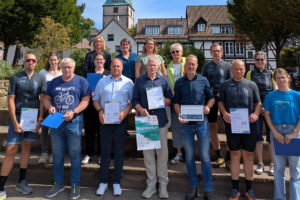 Die Organisatoren, Sponsoren und ausgezeichneten Radfahrerinnen und Radfahrer des STADTRADELN 2026 im Landkreis Holzminden posieren am Weserkai vor der Treppe des Duftgartens mit diesem und der Lutherkirche im Hintergrund.